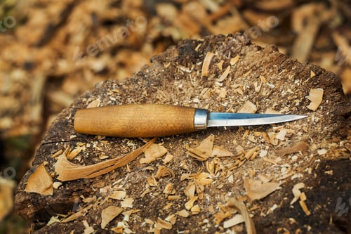 Preview: A carving knife with wooden handle lying on splitting block covered in wood shavings.