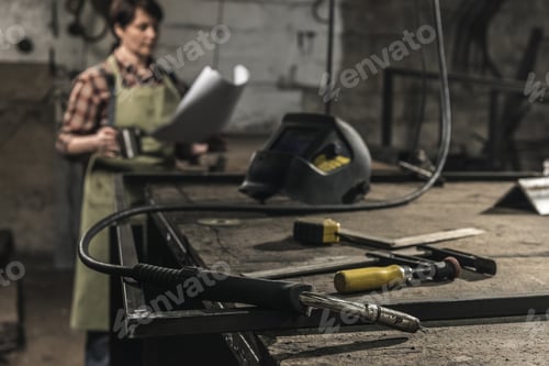 Preview: selective focus of welder with cup of hot drink reading papers in workshop