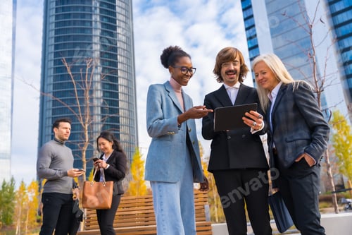 Preview: Multi-ethnic business colleagues or executives, looking at technology, glass office buildings