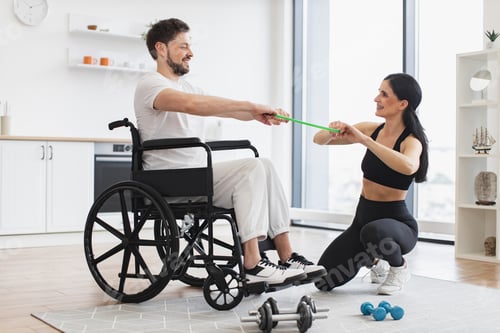 Preview: Physiotherapist helping adult man in wheelchair to workout with stretching bands