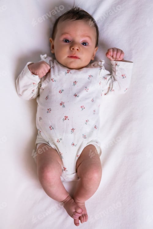 Preview: Newborn baby girl lying on white bedding overhead