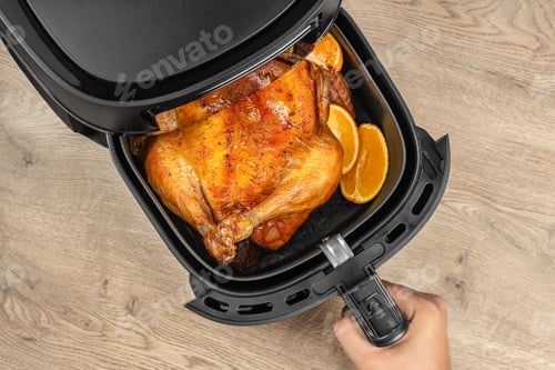 Preview: Whole roasted chicken with oranges in air fryer on wooden table, top view, free space for text