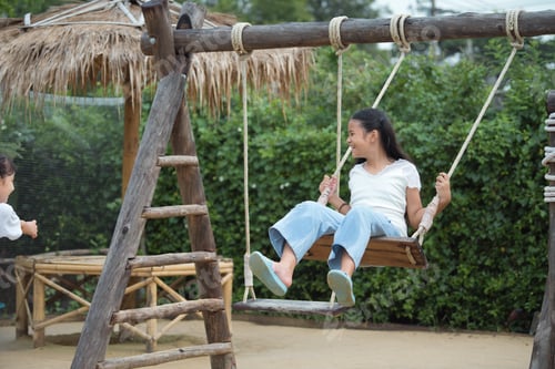 Preview: Happy girl playing on the wooden swing in the playground.
