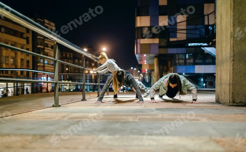 Preview: Female sport team doing push ups during training on the city at night