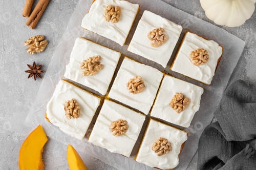 Preview: Spiced pumpkin cake with walnut and cream cheese frosting sliced into squares. Autumn dessert.