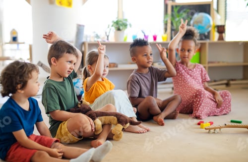 Preview: Group of small nursery school children sitting on floor indoors in classroom, raising hands