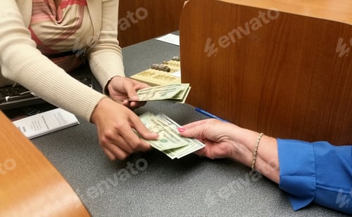 Preview: Womans hand reaches for money from teller at the bank for vacation cash and spending money.