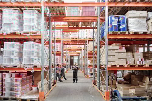 Preview: Young intercultural warehouse workers in uniform moving along large racks