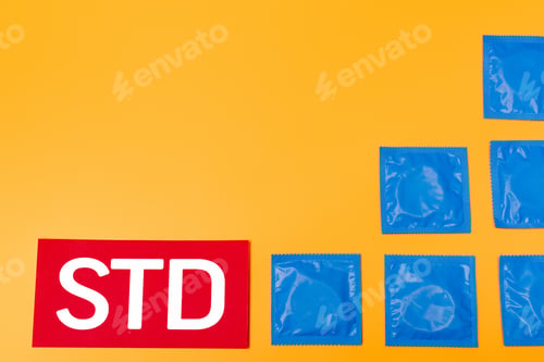 Preview: top view of packs with condoms near std lettering isolated on orange