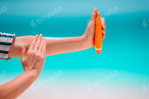 Preview: Beautiful young woman holding a suncream lying on tropical beach