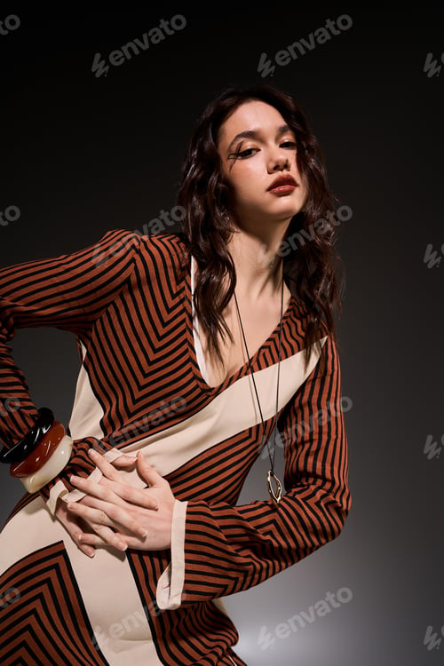 Preview: Stylish young woman poses elegantly in striped dress inside modern studio space