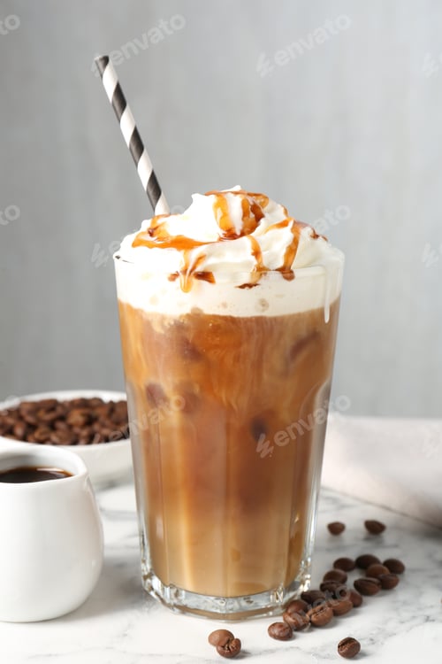 Preview: Tasty iced coffee with whipped cream, syrup and beans on white marble table