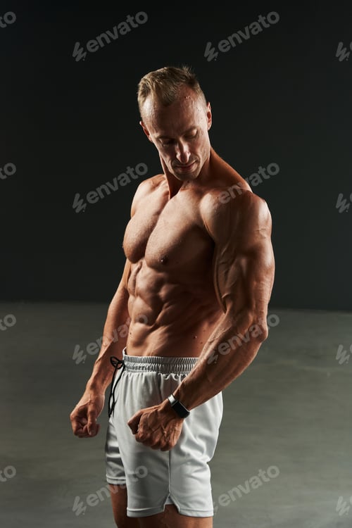 Preview: handsome caucasian man looks at his arm and biceps with protruding vein. ideal abdominal and chest