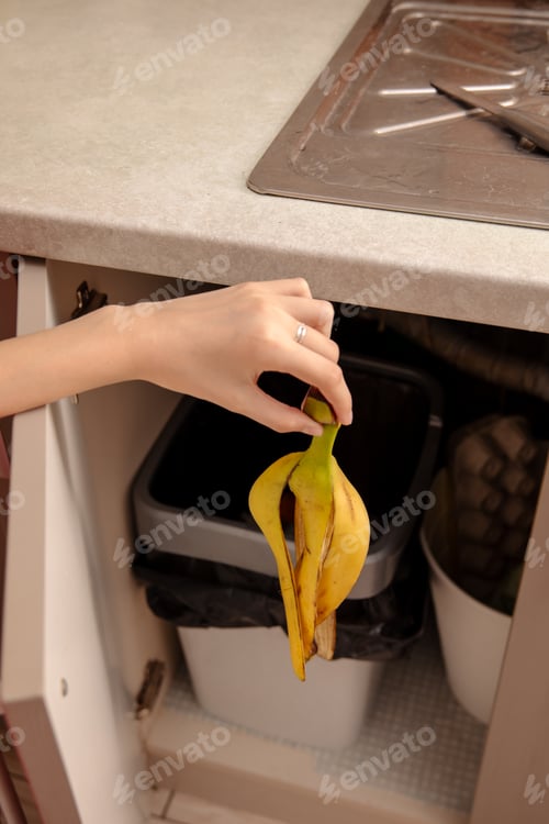 Preview: Woman putting banana peel in a trash bin. Kitchen and home
