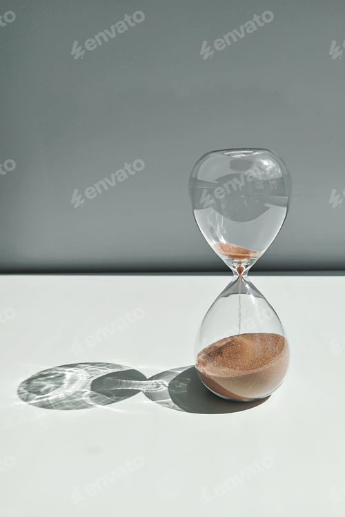 Preview: Glass sandglass on white table on gay background