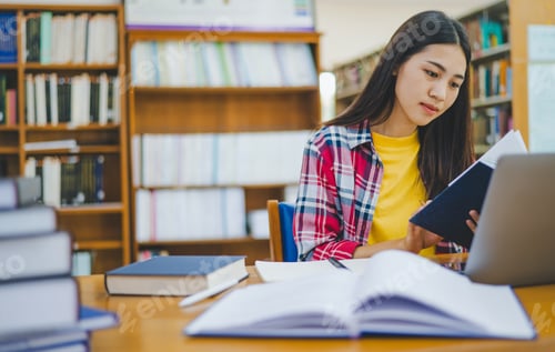 Preview: Female college student working on laptop and searching for books to study
