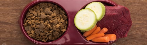 Preview: top view of dry pet food and raw meat with vegetables in bowl on wooden table, panoramic shot
