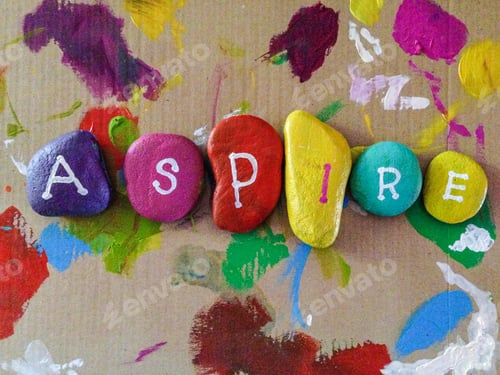 Preview: Art project aspire painted on rocks with bright colors and paint in background Inspiring words