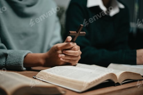 Preview: Group of Christians sit together and pray around a wooden table with blurred open Bible pages