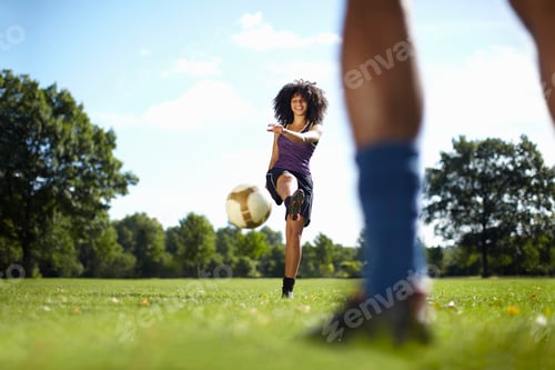Preview: Young woman kicking soccer ball toward boyfriend in park