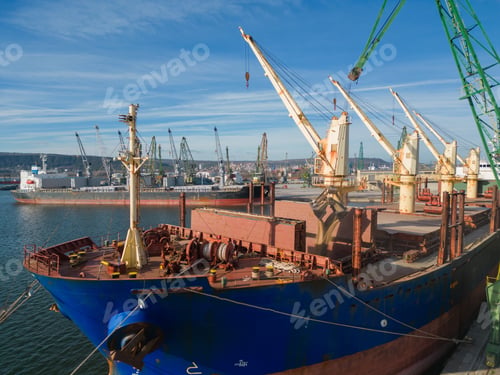 Preview: A bulk carrier ship loaded with grain is docked at a busy port, with workers and machinery seen in