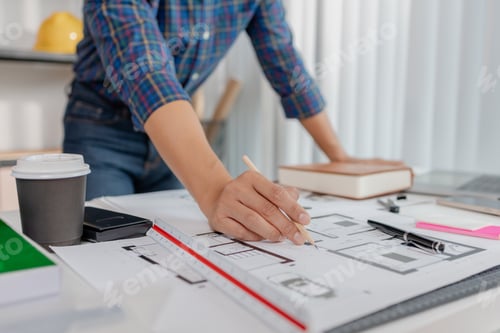 Preview: A young architect is multitasking at his desk, sketching blueprints