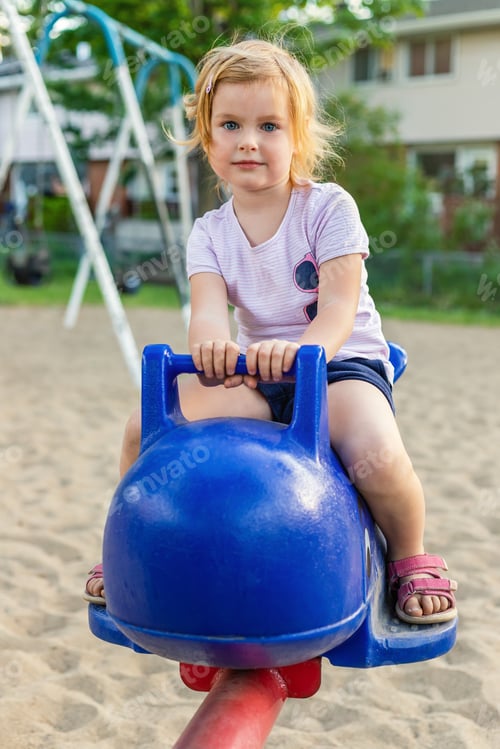 Preview: Little girl playing at playground in summer, sitting on carrousel