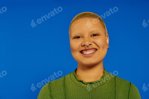 Preview: Young stylish woman with a gleaming smile stands against a vibrant blue backdrop