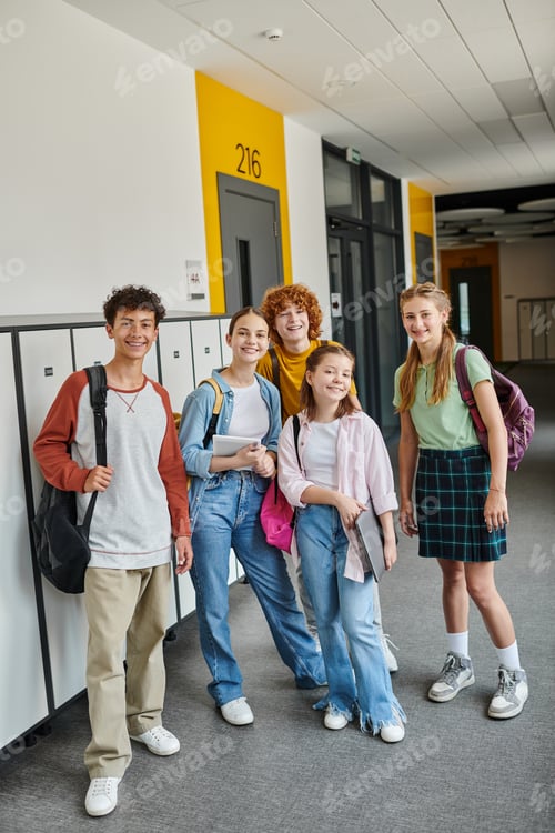 Preview: teenage schoolkids looking at camera and standing together in school hallway, teen classmates