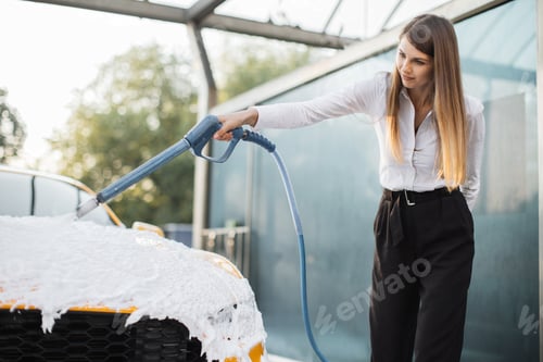 Preview: Young coucasian woman in business outfit, shirt and trousers washing her yellow car with foam