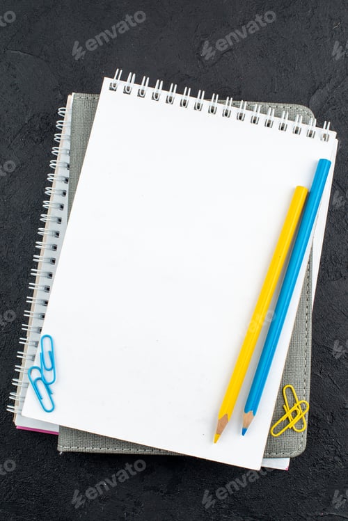 Preview: top view office stuffs yellow and blue pencils on notepads gem clips on dark background
