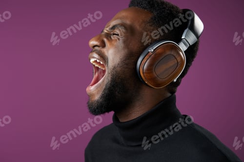 Preview: Young Black man enjoying music with stylish headphones, expressing emotions in a vibrant purple