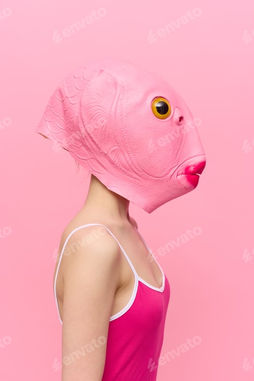 Preview: Funny crazy woman on a pink background standing in a fish head mask on a pink background, conceptual
