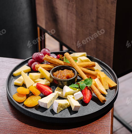 Preview: Cheese and fruit platter served on a black plate in a cozy restaurant