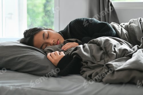 Preview: Carefree teenage woman sleeping in comfortable bed and covered with blanket.