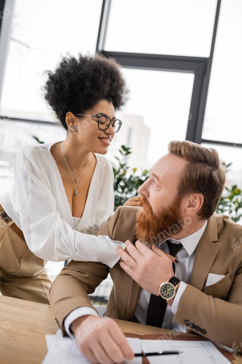 Preview: smiling african american businesswoman seducing and touching coworker in office