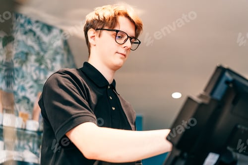 Preview: Young waiter serving customer at cash point in cafe. Man working with POS terminal. Cashier, barista