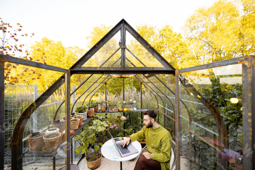 Preview: Man works remotely on laptop in glasshouse at backyard