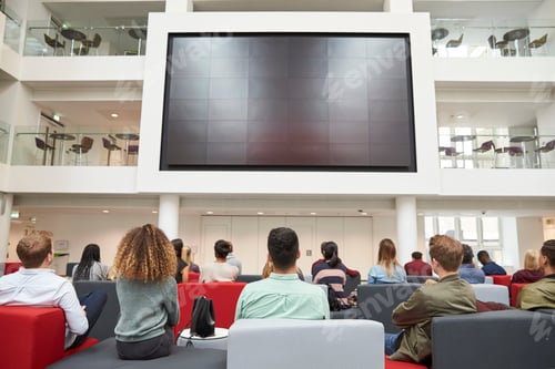 Preview: Students watching big screen in university atrium, back view