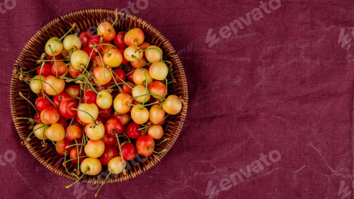 Preview: top view of basket full of yellow and red cherries on left side and bordo cloth background with copy