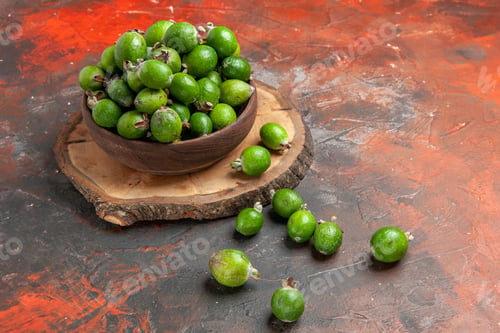 Preview: Side view of natural fresh green feijoas in a brown pot on wooden tray on dark background