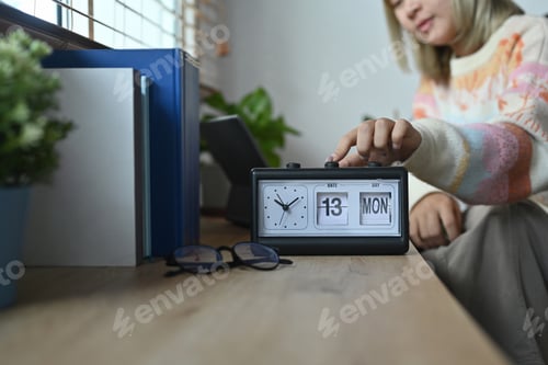 Preview: Smiling woman in warm sweater hand adjusting or changing the time on clock.