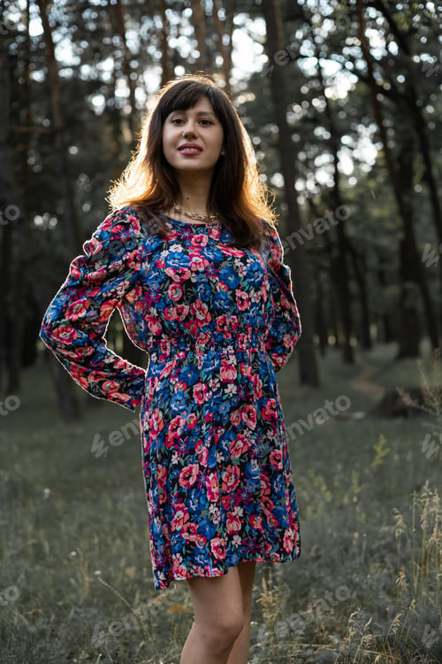 Preview: Woman breathing fresh air in green forest in summer wearing dress at sunset.