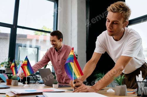 Preview: A joyful moment shared by a handsome gay couple decorating their workspace with pride flags