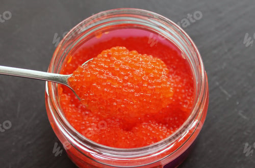 Preview: Red trout caviar in a glass jar with a spoon.