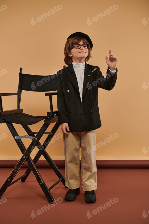 Preview: inspired boy stands proudly next to director chair, with a big smile on face showing idea sign