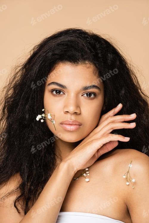 Preview: young african american woman with small gypsophila flowers on face isolated on beige