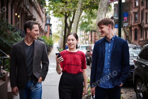 Preview: Two young men and a young woman walking down a city street looking at a cellphone.