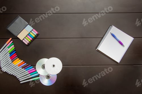 Preview: Top view of colored markers, CD disk, sticky notes and a notebook on a brown surface with copy space