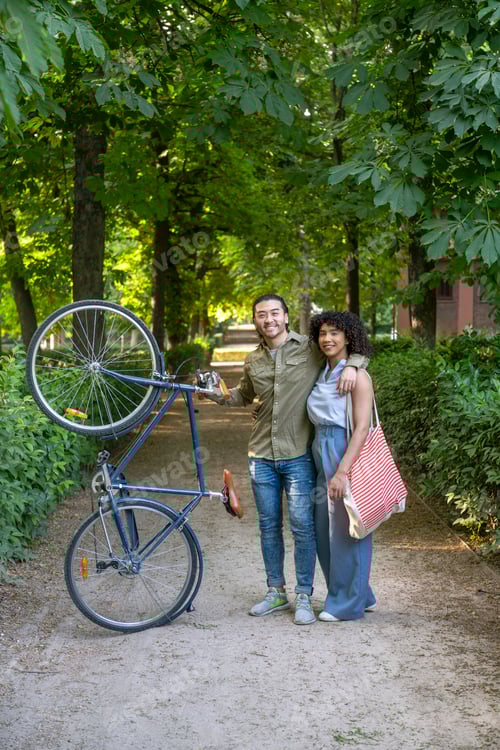 Preview: Interracial couple walking bicycle in park hugging